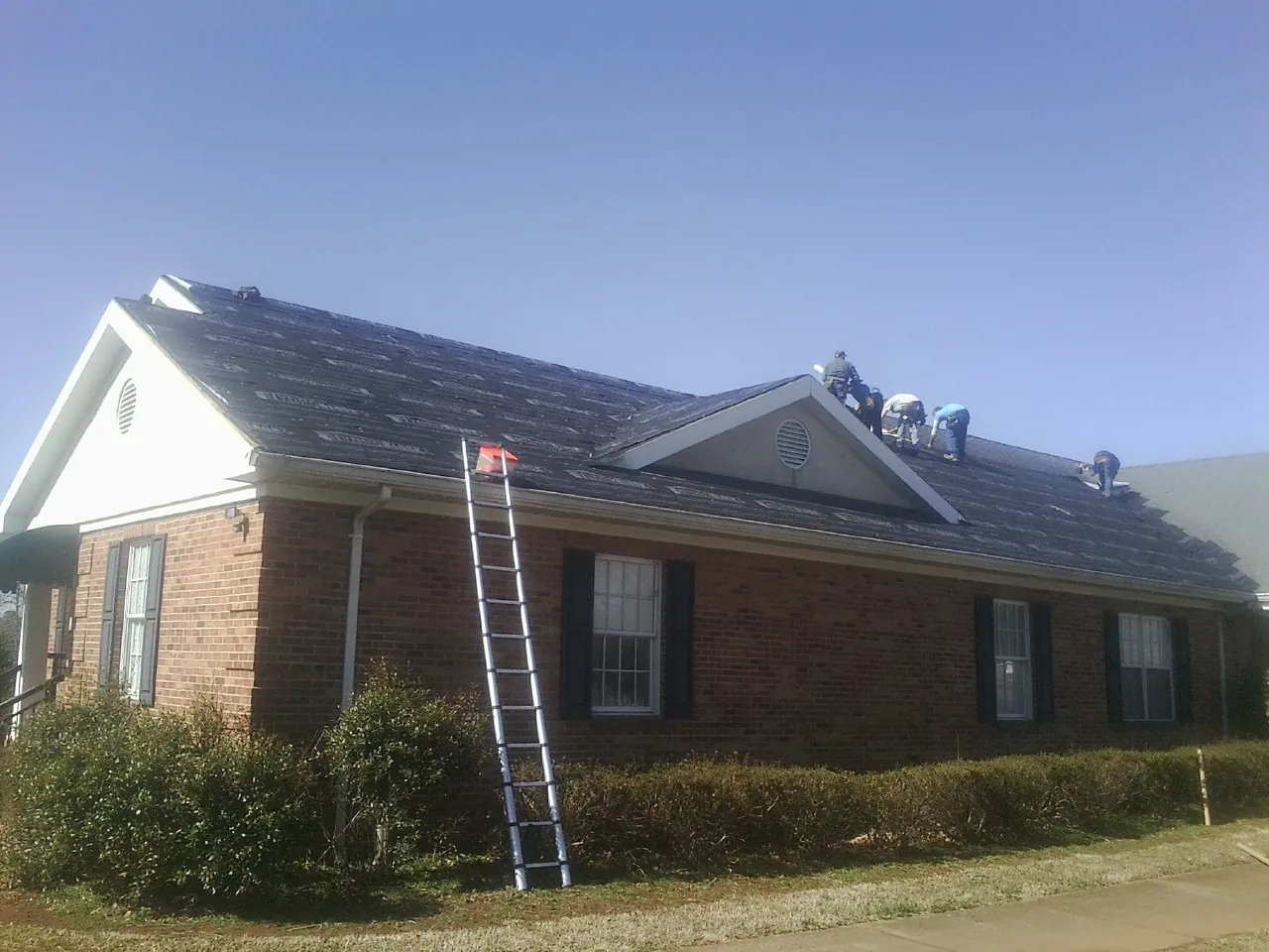 Crew tearing shingles off a brick ranch roof with a ladder set — Emergency Roof Repair work by our crew in Lookout Mountain