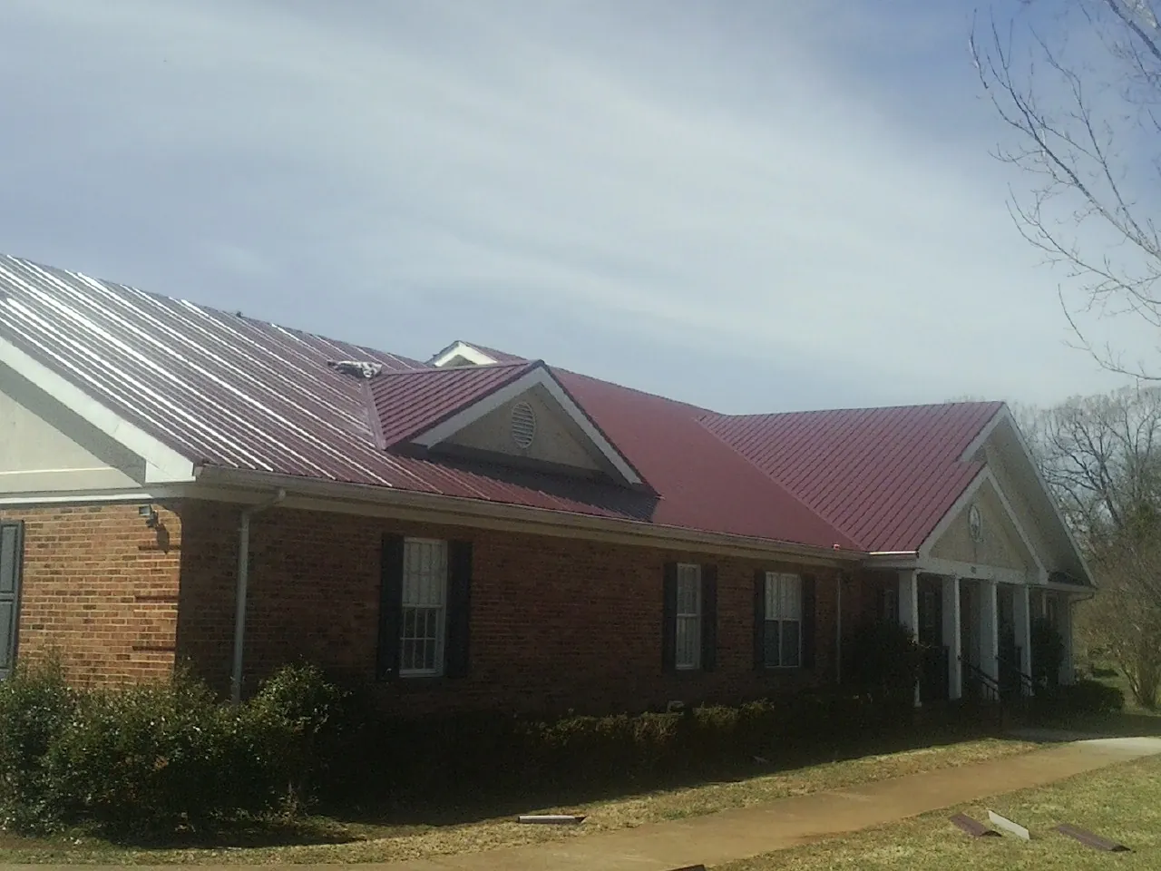 Red metal roof with gabled entries on a long brick building, from a Hail Damage Roof Repair job in Lookout Mountain