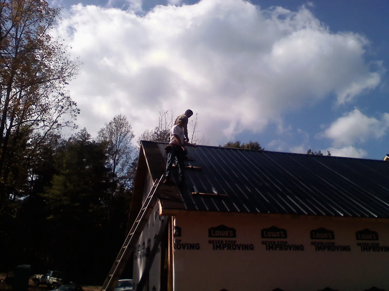 Roofer fastening dark metal panels high against a cloudy sky, from a Roof Inspection job in Lookout Mountain